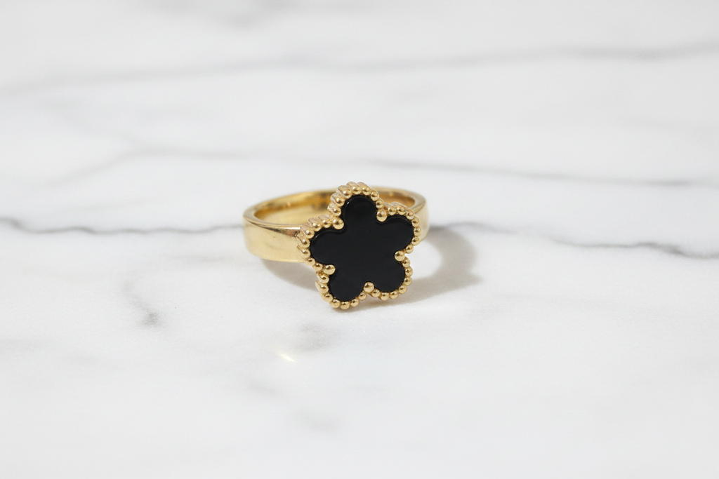 Anillo trébol negro dorado sobre mármol