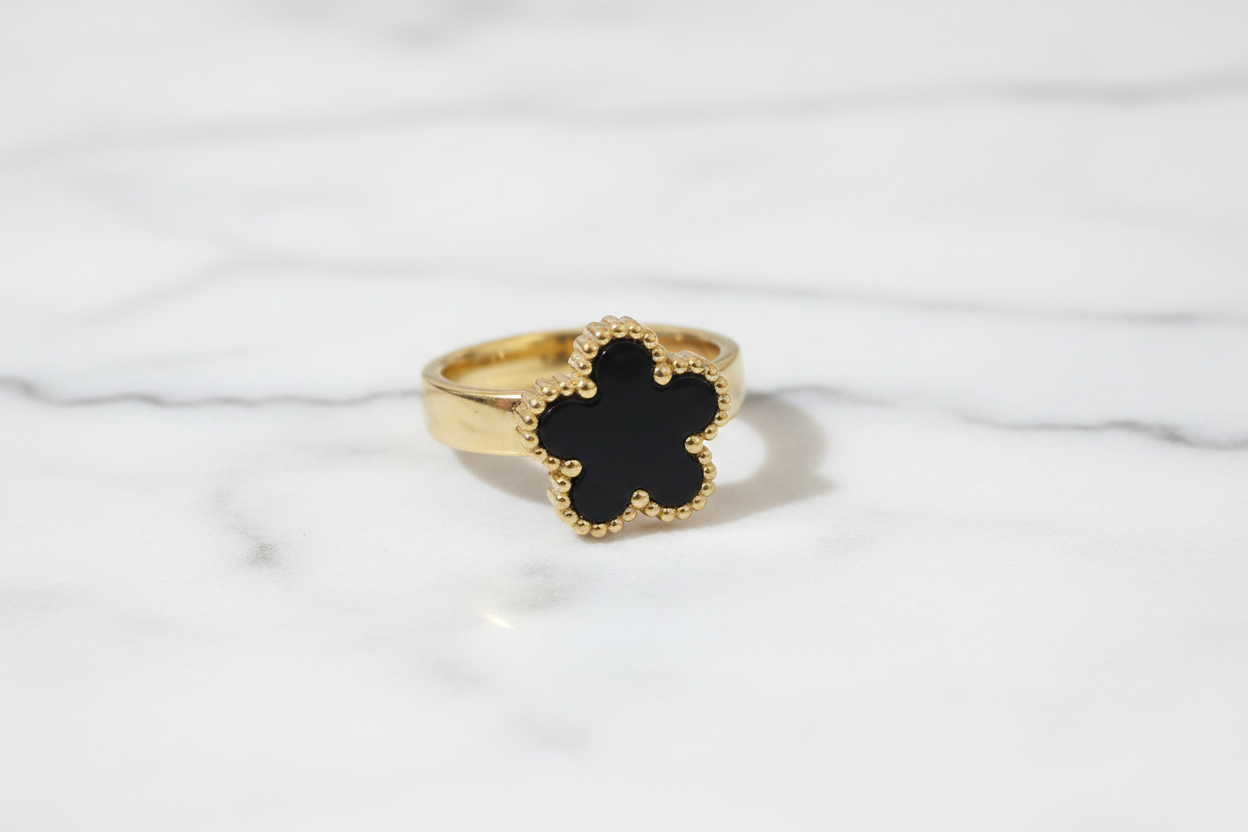 Anillo trébol negro dorado sobre mármol